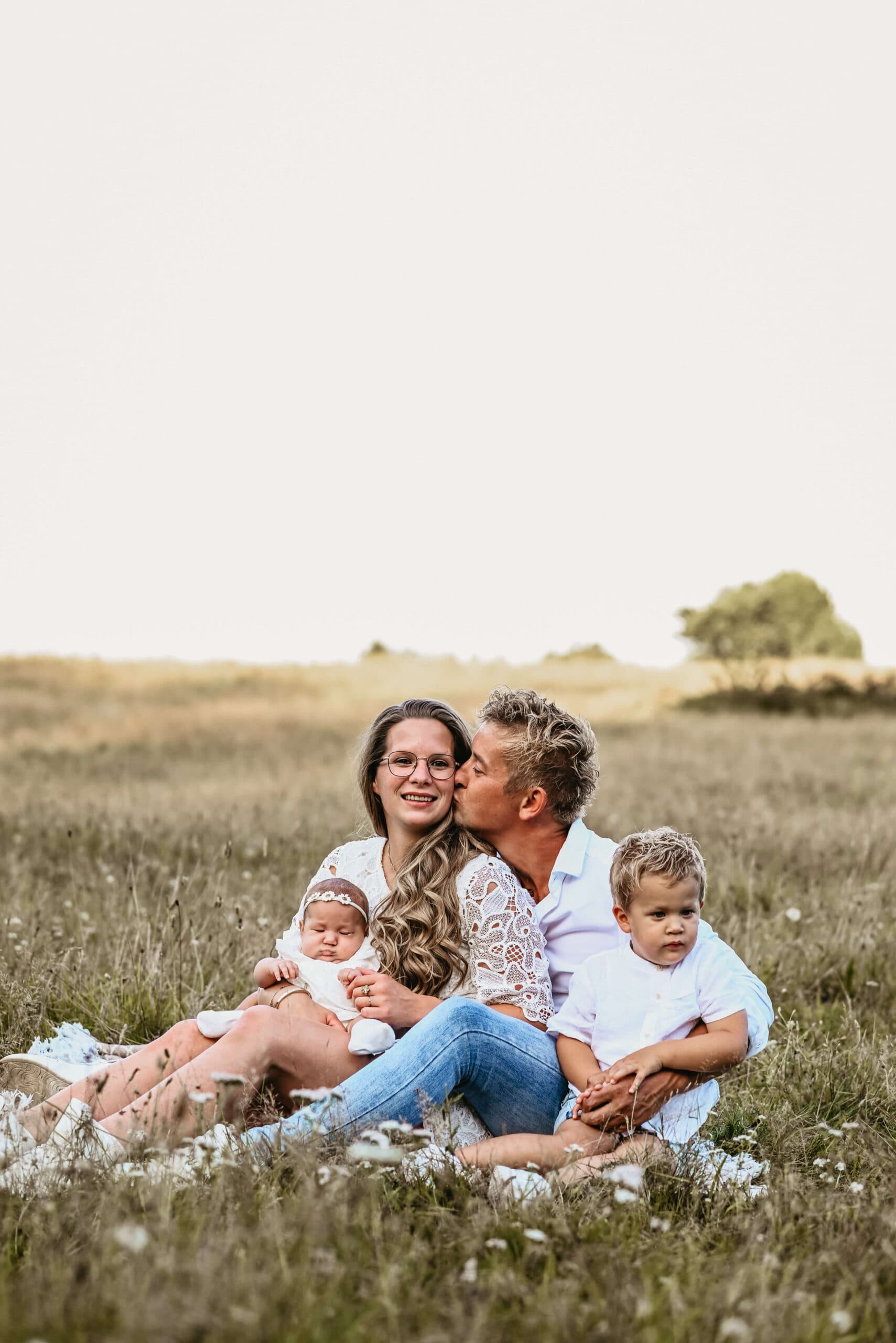 Gezin zit samen in bloemenveld bij avondzon – Studio Roos Fotografie