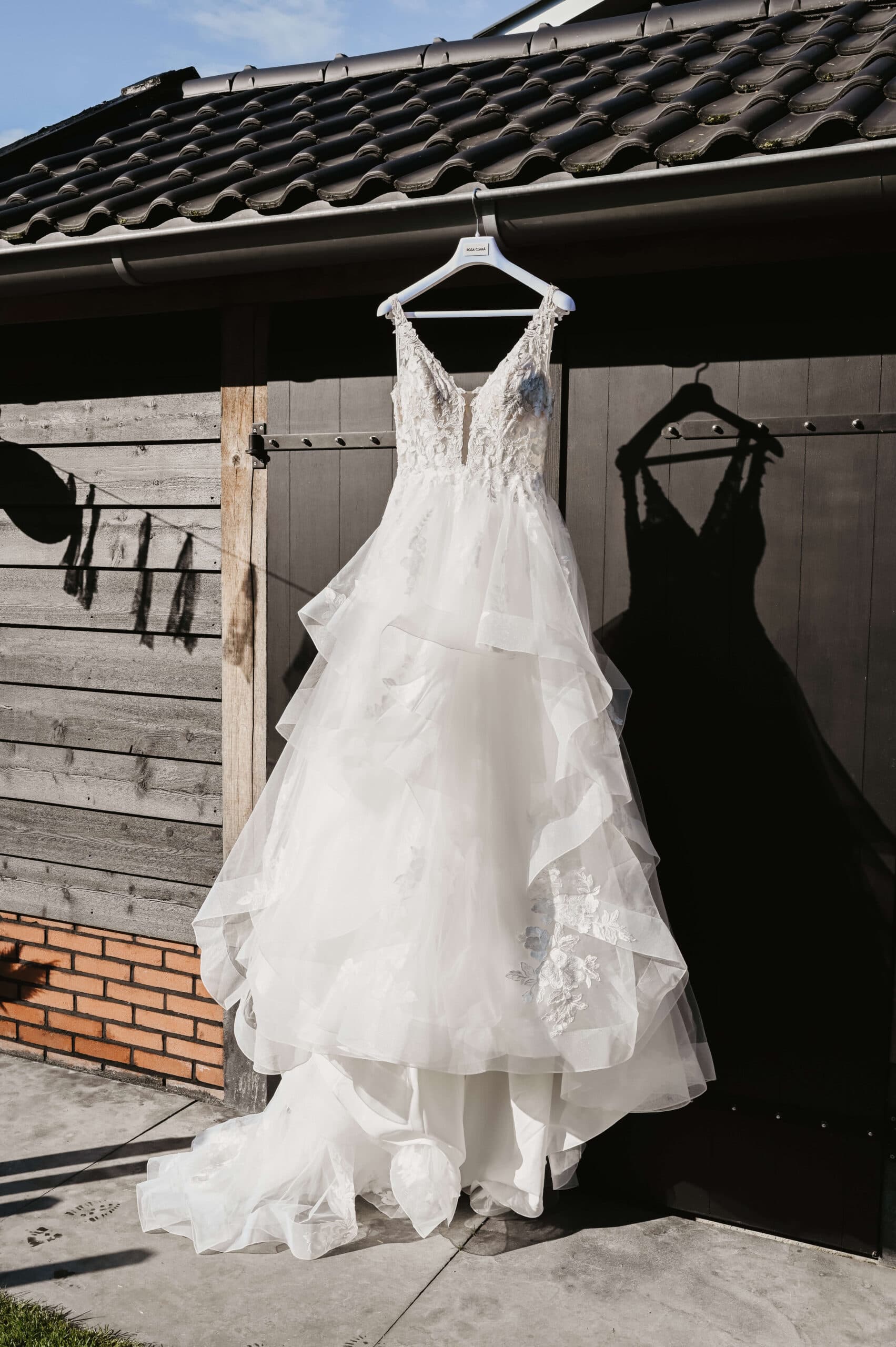 Trouwjurk hangt aan houten schuurdeur – Studio Roos Fotografie