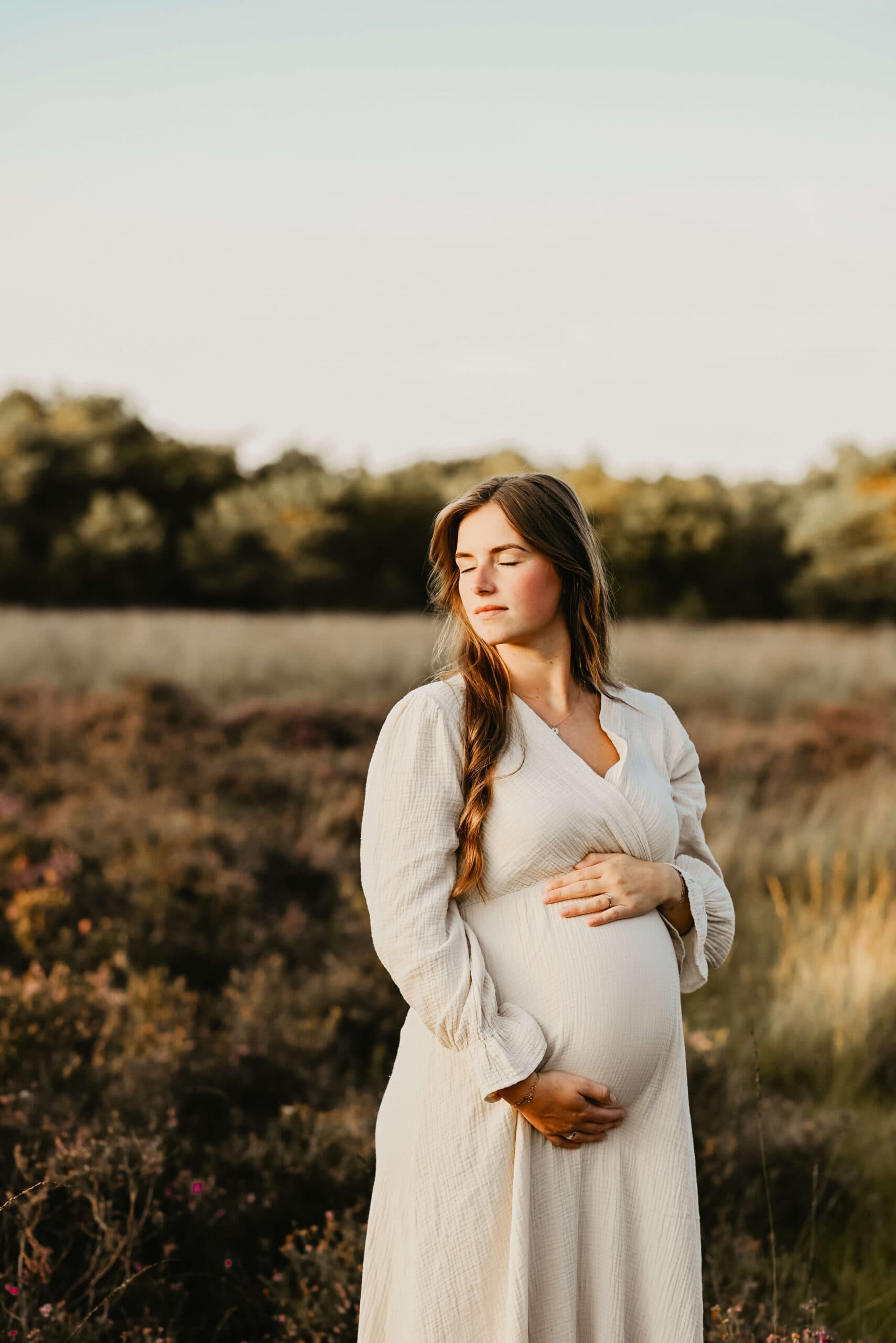 Zwangere vrouw houdt haar buik vast in avondlicht – Studio Roos Fotografie