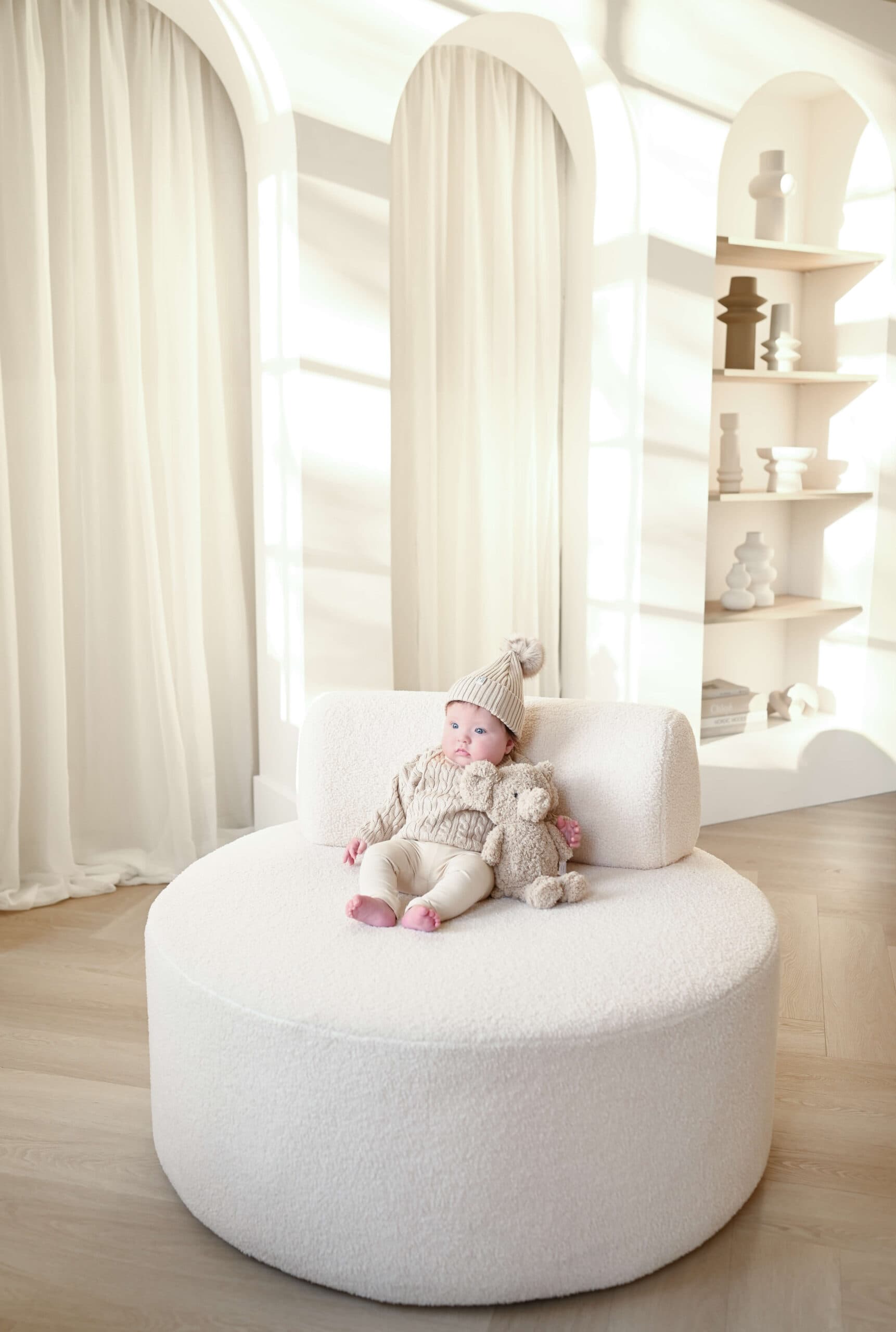 Baby in gebreid pakje op ronde poef in studio – Studio Roos Fotografie