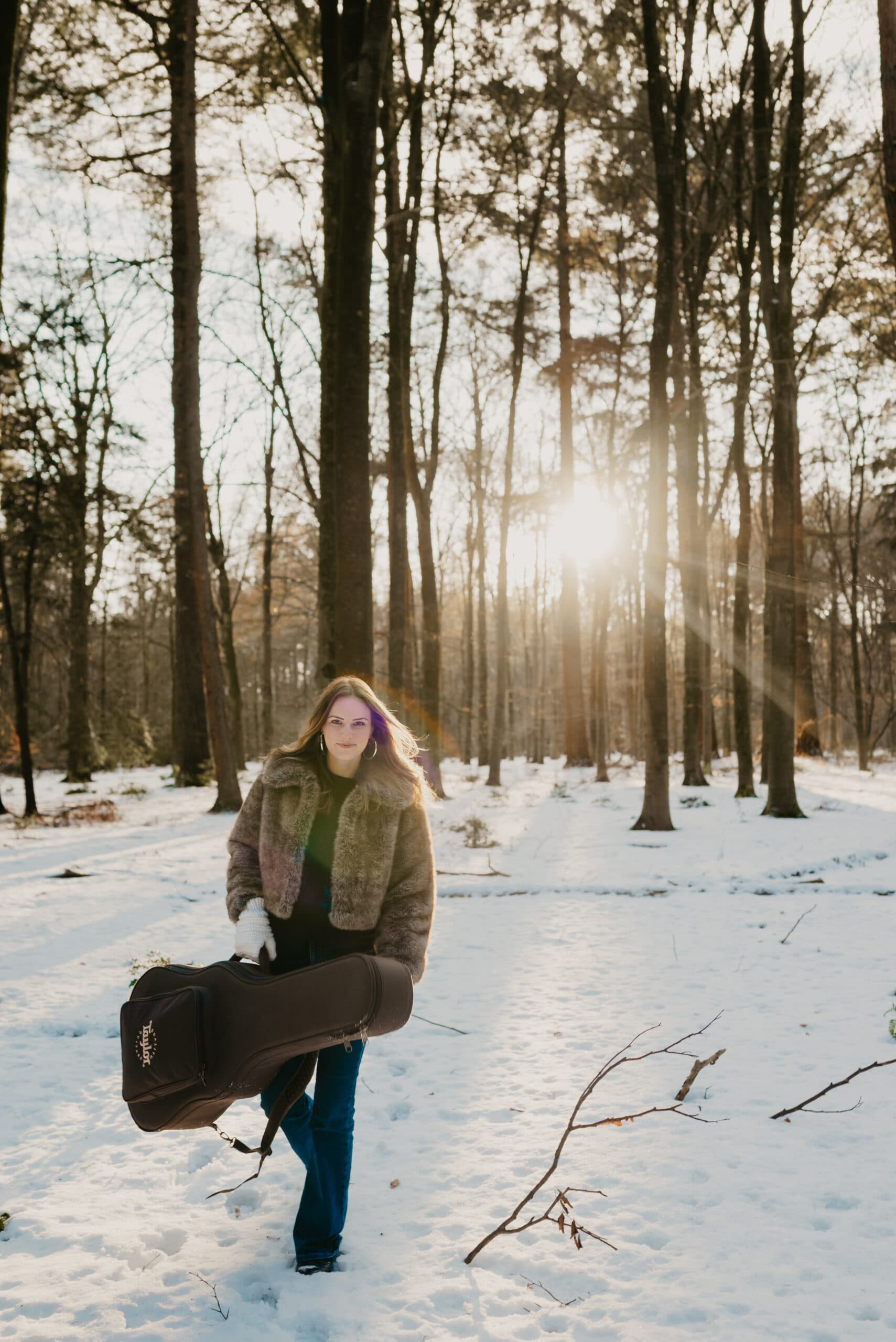 Muzikante loopt met gitaarkoffer door winterzon in bos – Studio Roos Fotografie