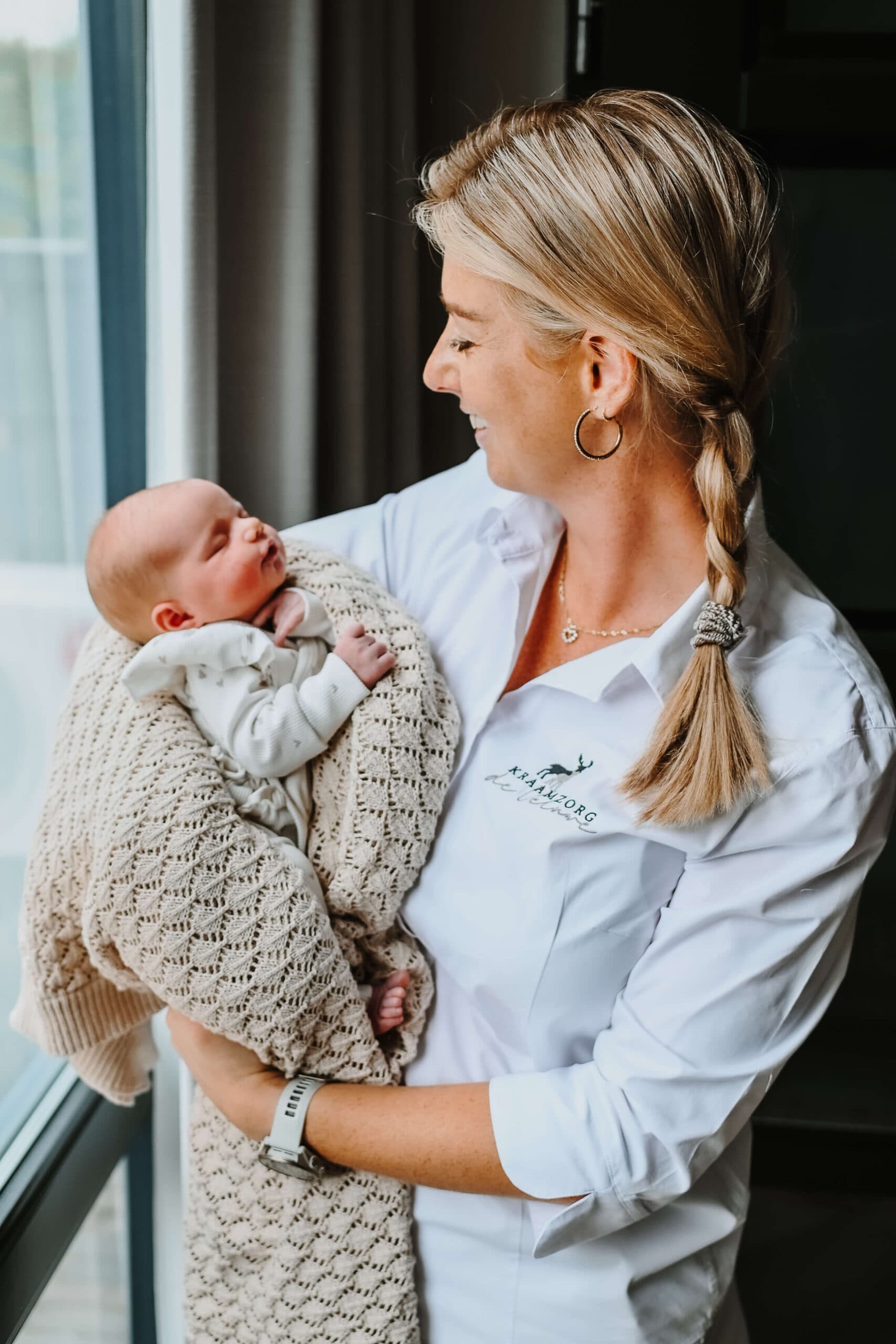 Kraamverzorgster met newborn bij het raam – Studio Roos Fotografie