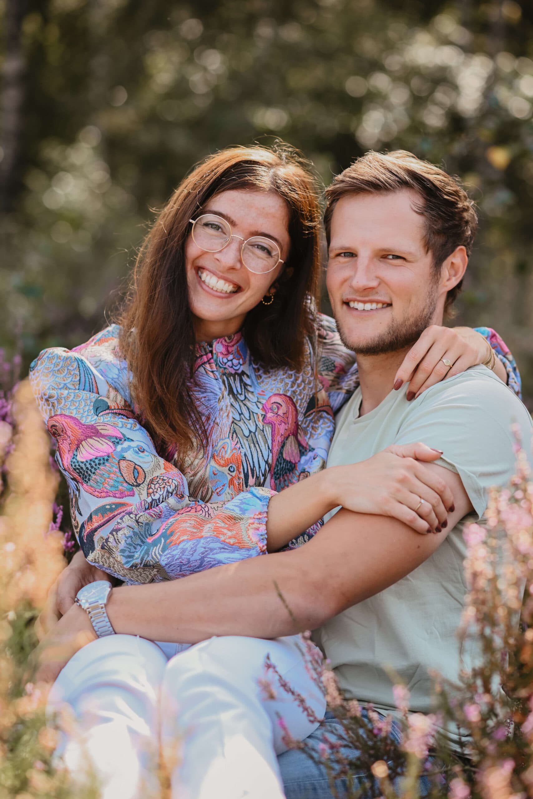 Stel zit dicht tegen elkaar tussen bloeiende heide – Studio Roos Fotografie