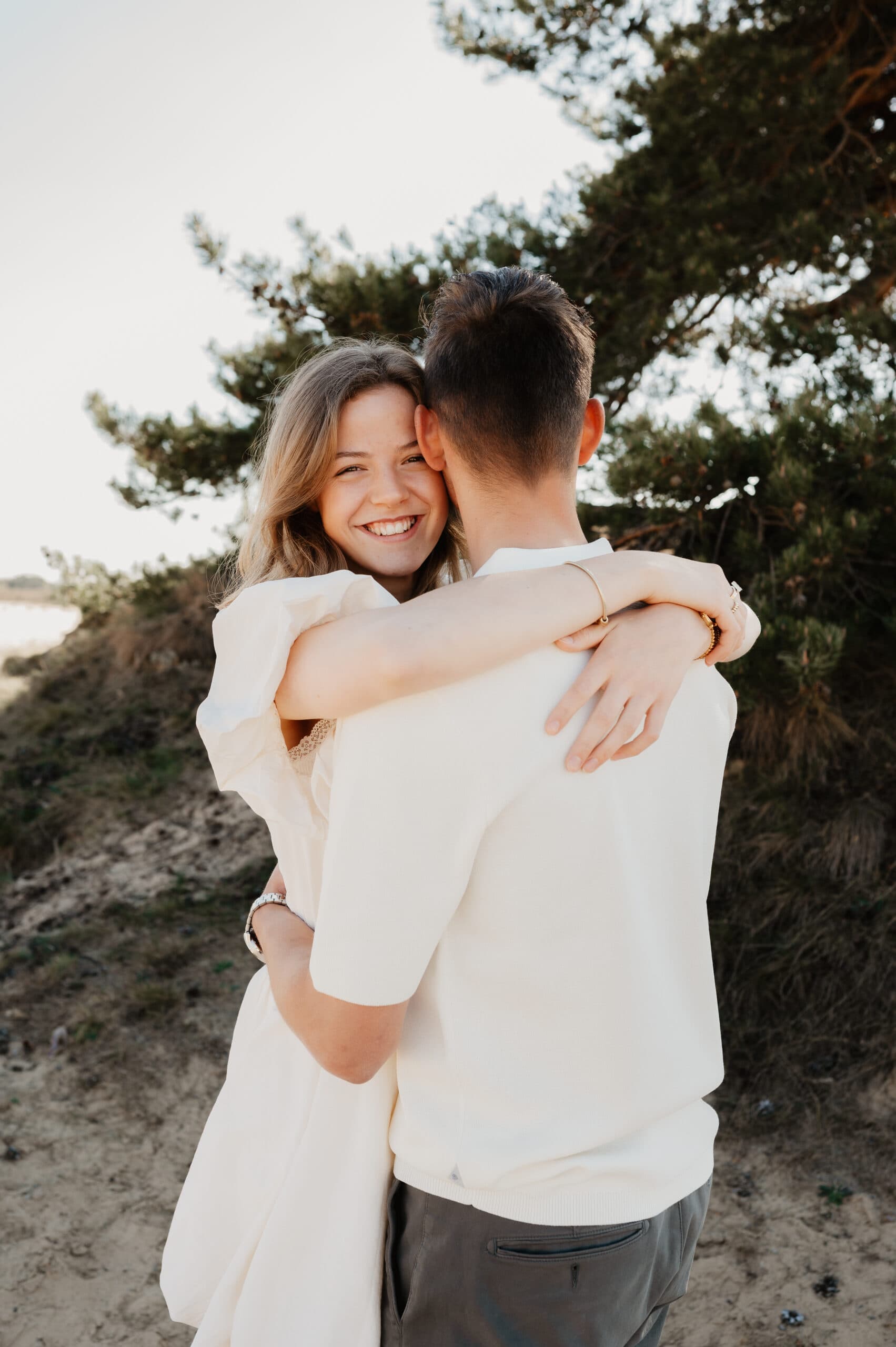 Lachende vrouw omhelst haar partner in de duinen – Studio Roos Fotografie